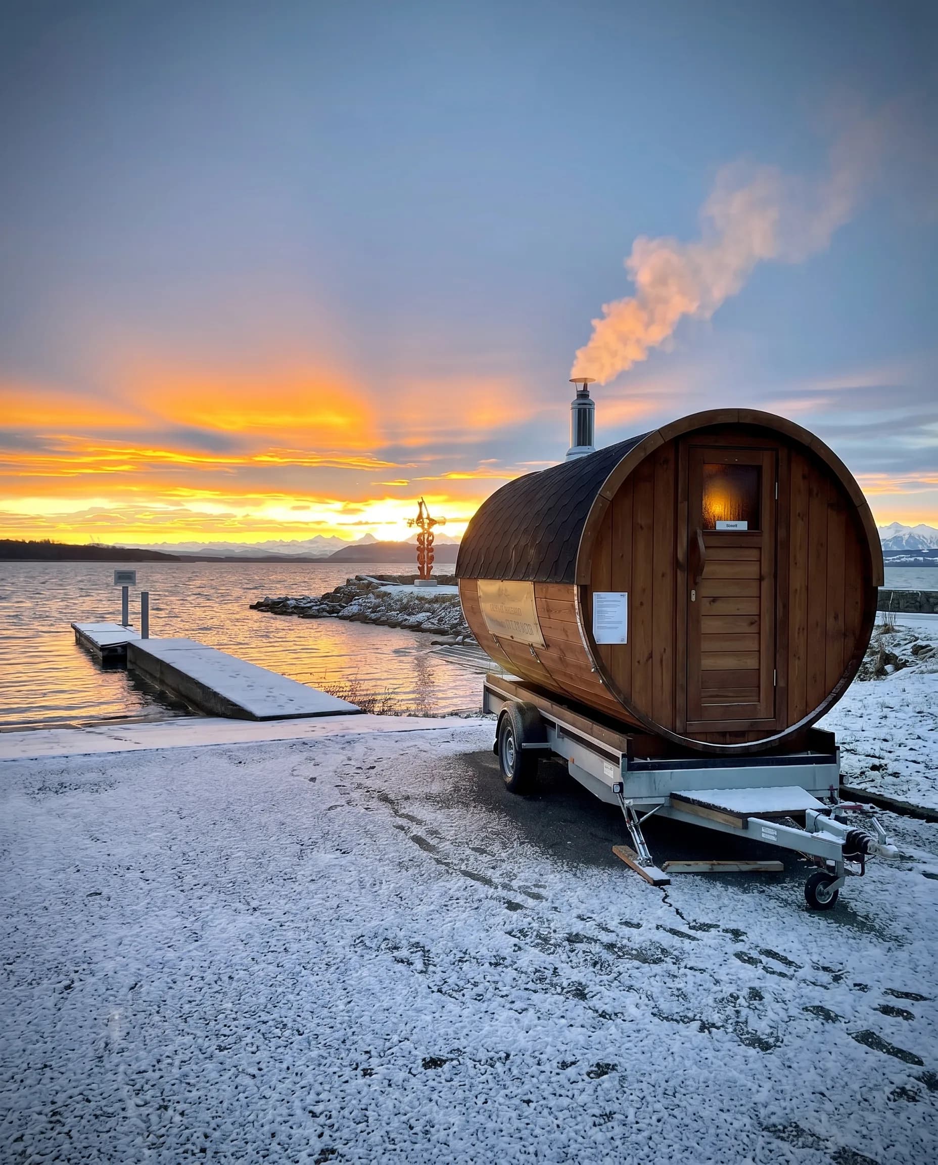 Sauna tonneau au bord du lac enneigé de Neuchâtel au coucher du soleil